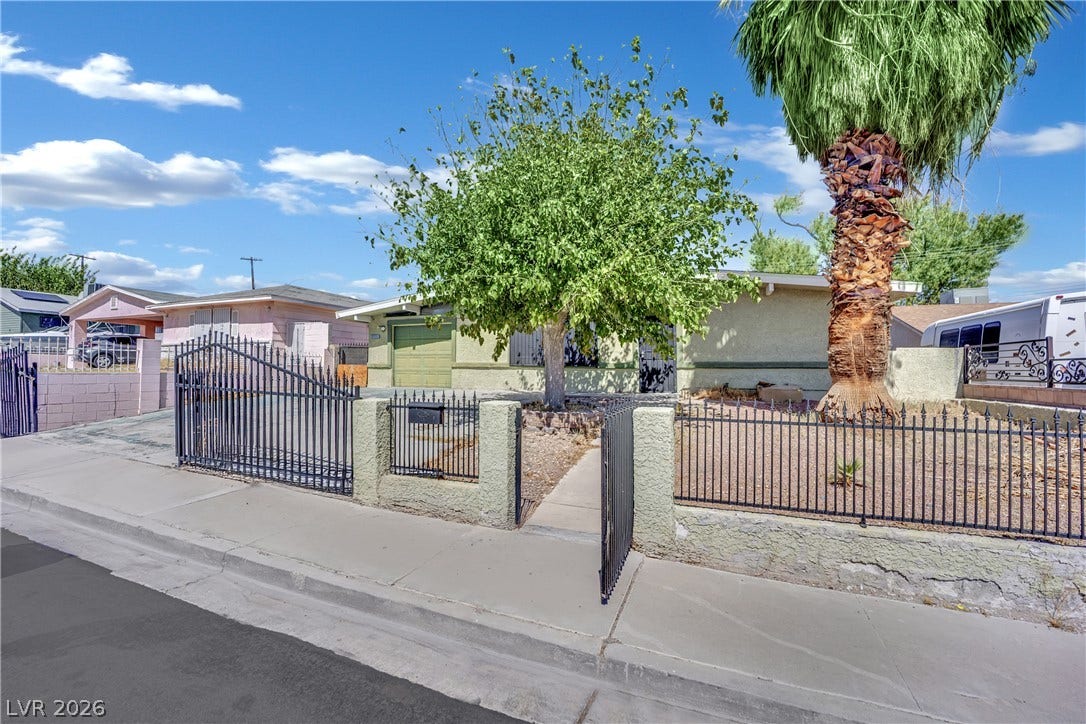 Secure wrought iron fencing and mature trees frame the welcoming entrance of this single-story home.