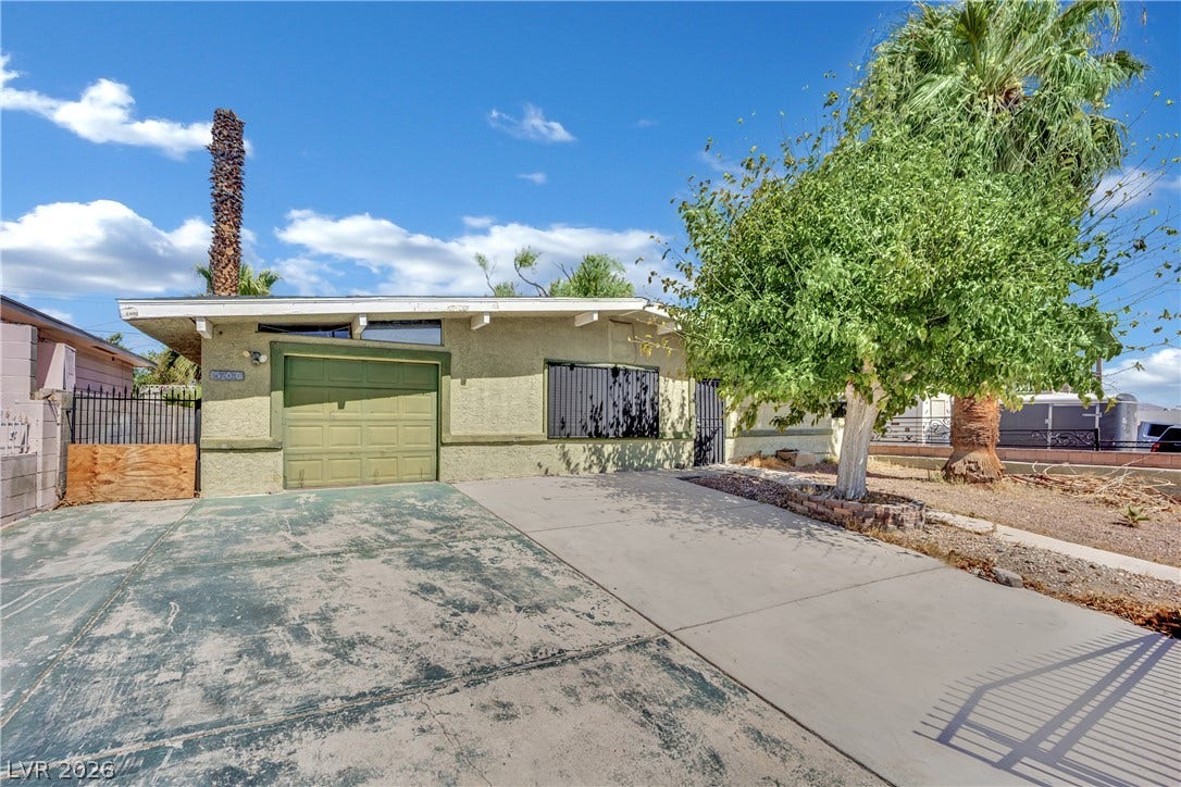 A spacious concrete driveway leads toward the single-car garage of this single-story midcentury residence.