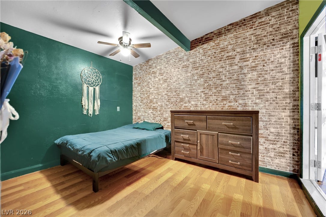 Exposed brick accents and rich wood-style flooring create a cozy, character-filled bedroom atmosphere.