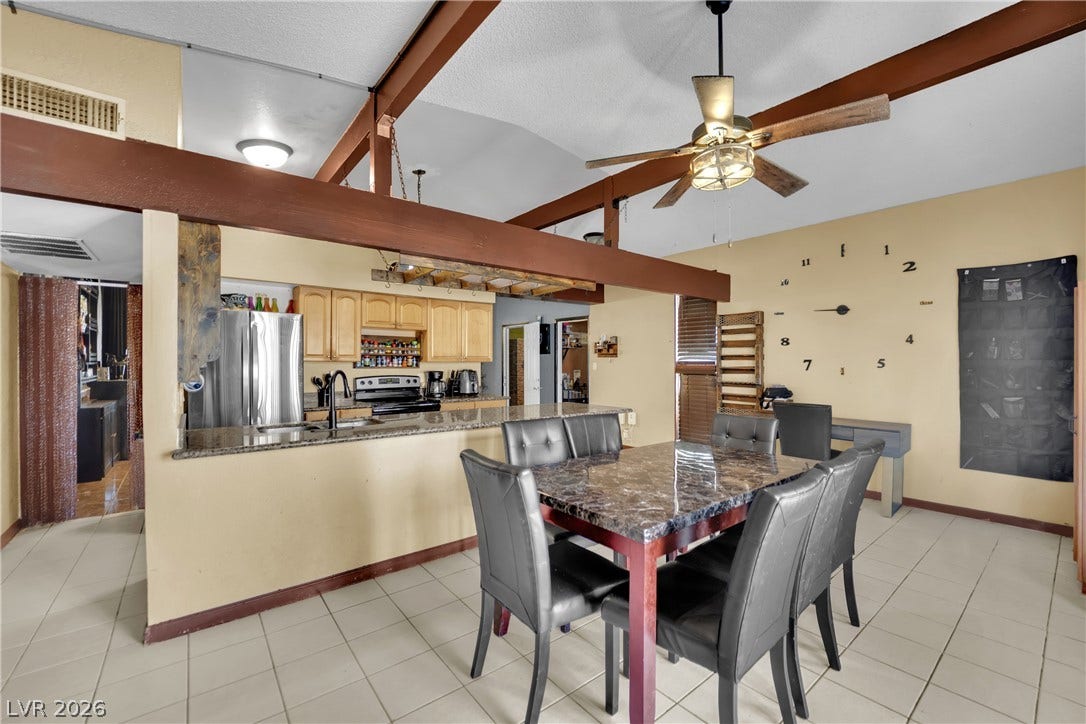 Exposed wooden ceiling beams and tile flooring define this open dining and kitchen area.