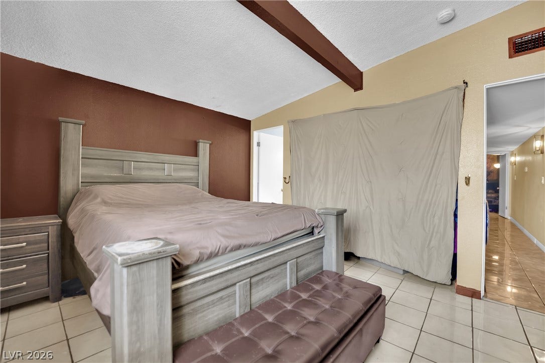 Vaulted ceilings with a prominent wood beam highlight this tiled primary bedroom.