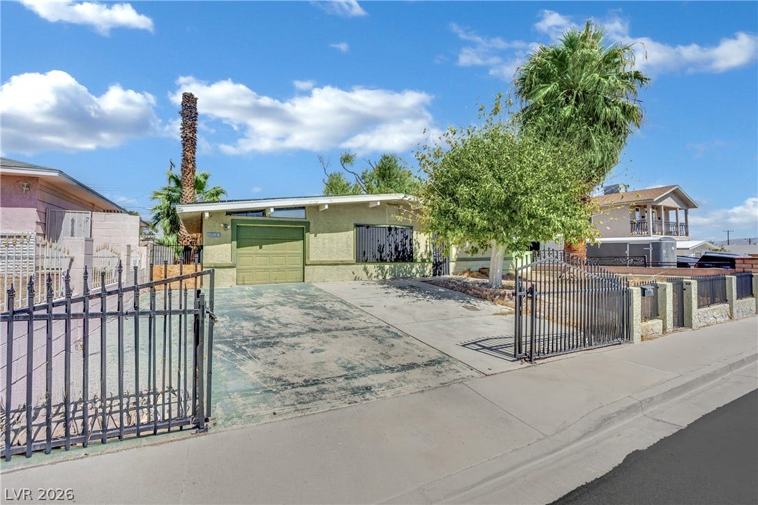 Secured gates frame the paved driveway leading toward a classic single-story midcentury modern home.