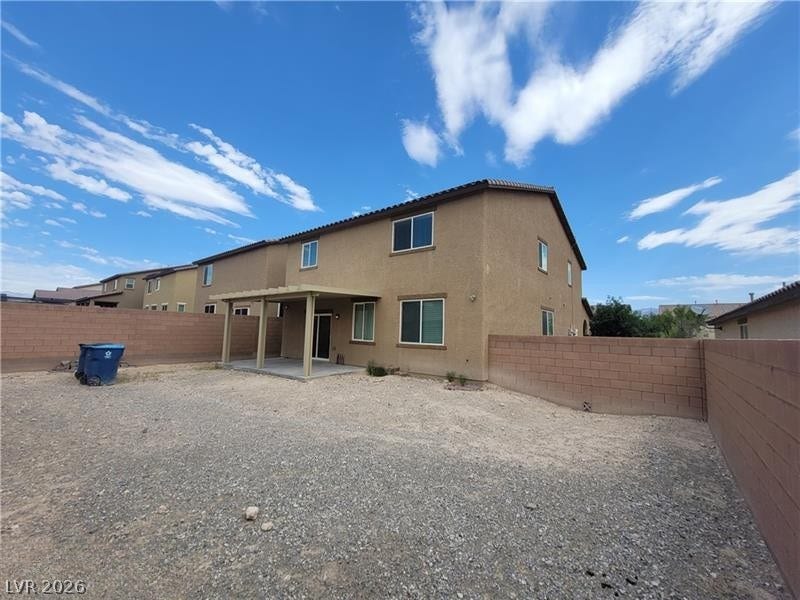 Block fencing encloses a spacious gravel yard featuring a covered patio structure.