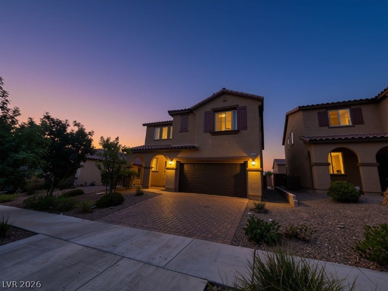 A paved driveway leads to a modern two-story home with stucco siding under twilight skies.