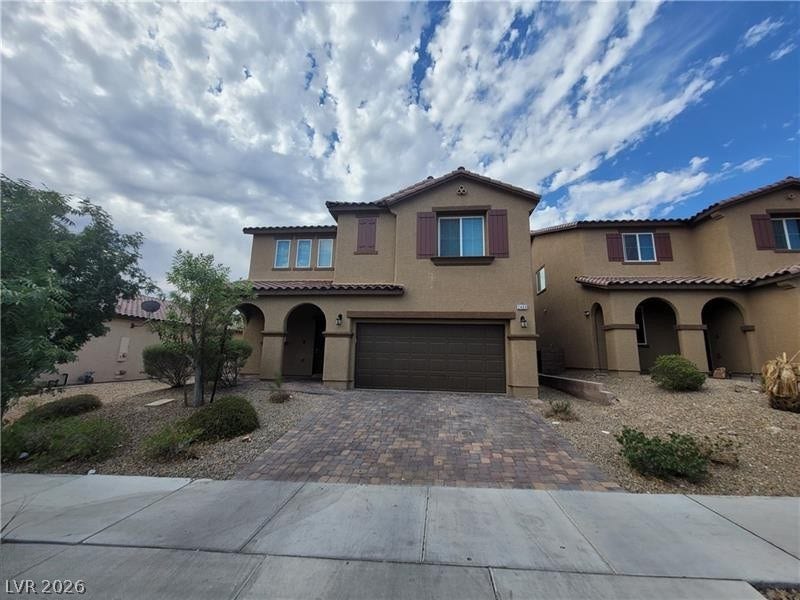 Arched entryways and a paved driveway enhance this stucco home with tile roofing.