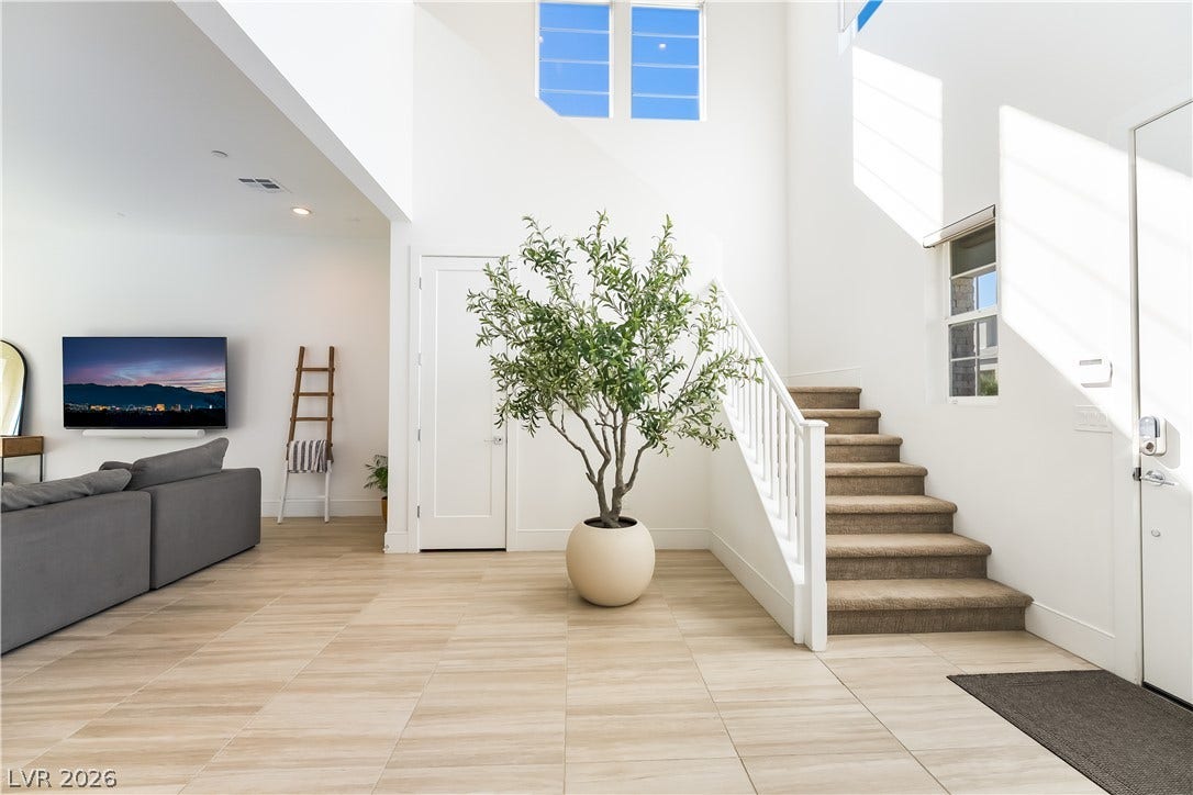 10143 Bismarck Palms Avenue, Las Vegas, NV 89166 Double-height ceilings and tall windows illuminate a welcoming tiled entryway with staircase access.