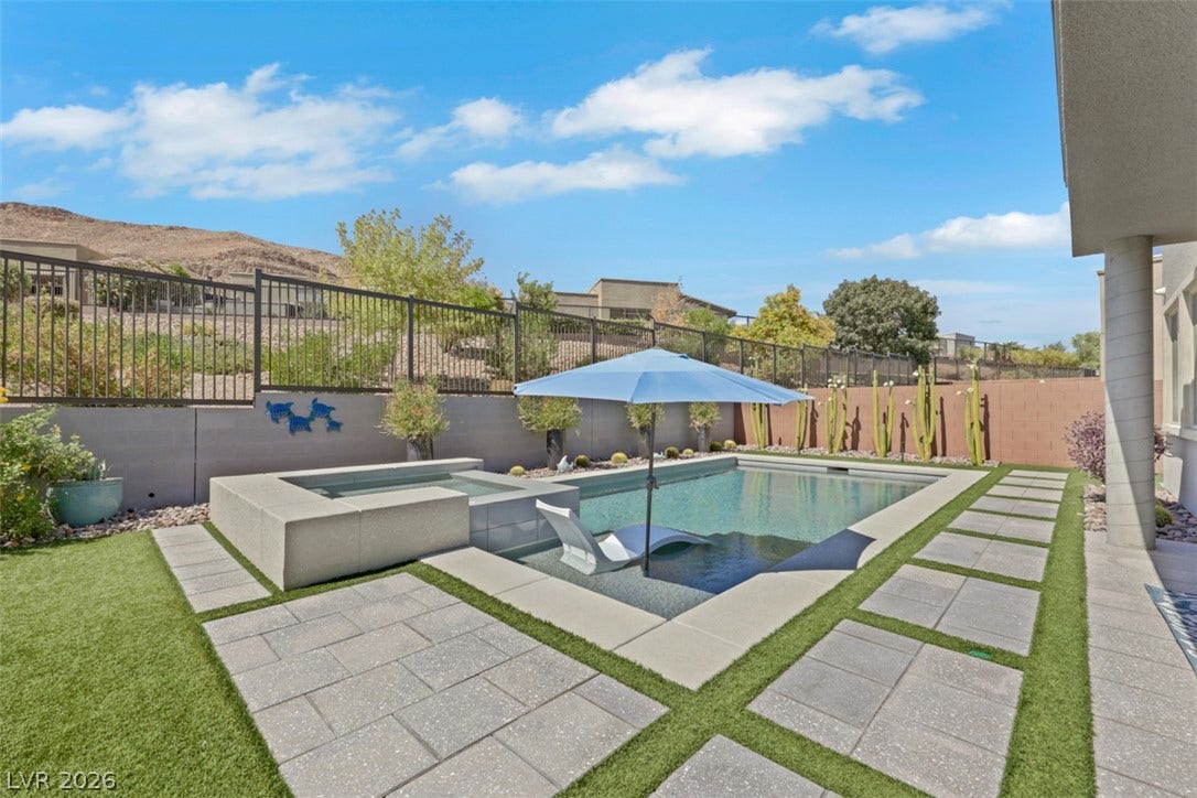 Inviting backyard pool and spa featuring a Baja wet deck with space for an umbrella and lounge chairs.