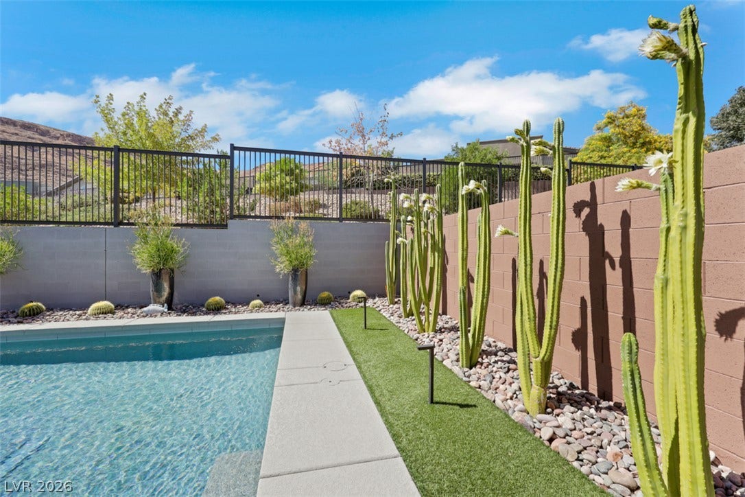 Blooming Cacti line the perimeter wall adjacent to a sparkling pool in this desert backyard.