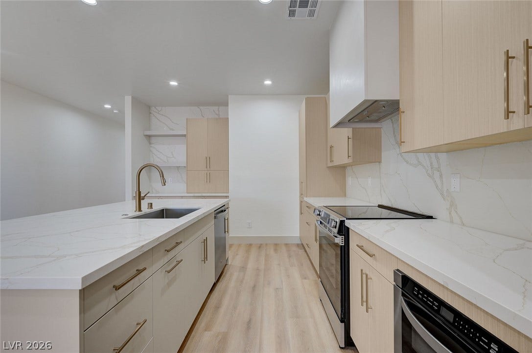 A spacious kitchen features light wood cabinetry, stone countertops, and a modern island.