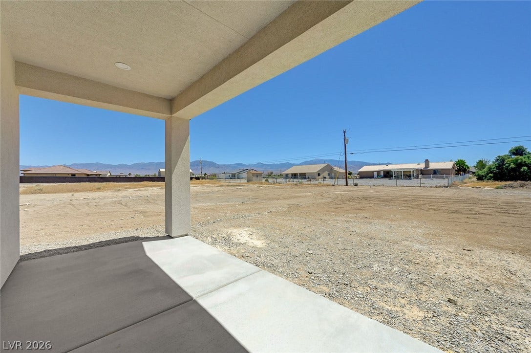 A covered concrete patio overlooks a wide backyard space with distant mountain views.