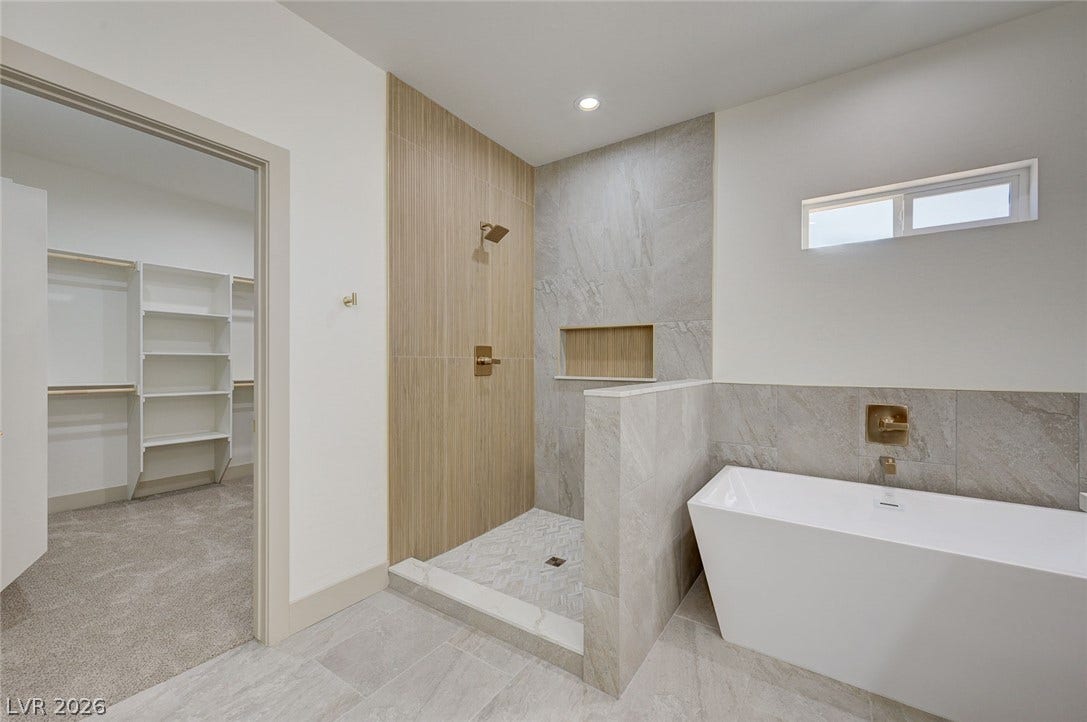 Modern stone tilework frames a freestanding soaking tub next to a walk-in shower.