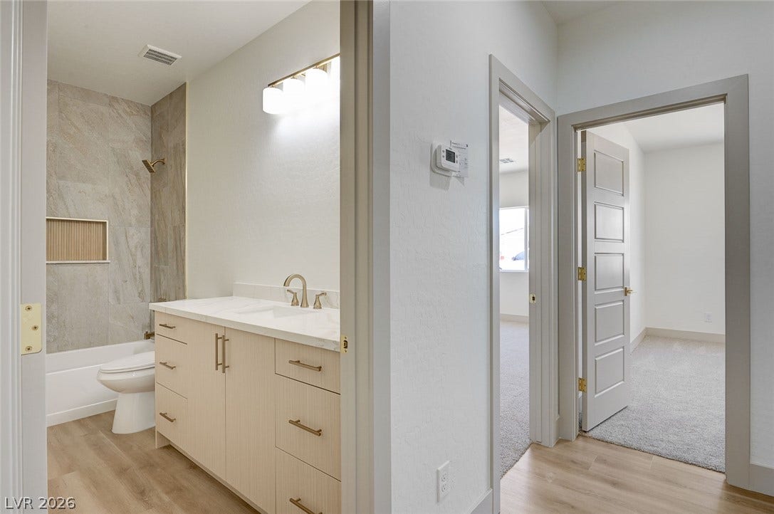 Smooth wood floors lead to a sleek bathroom featuring modern stone counters and tile surrounds.