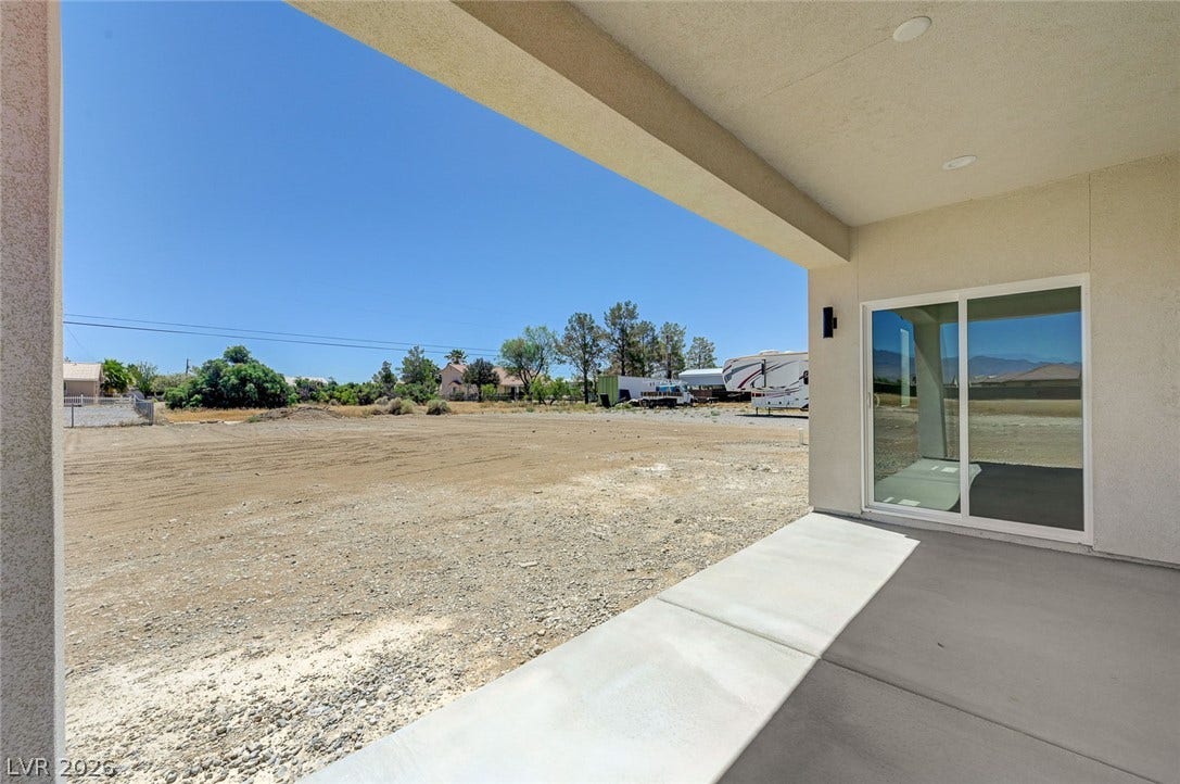 Shaded concrete patio looks out over a vast yard under clear blue skies.