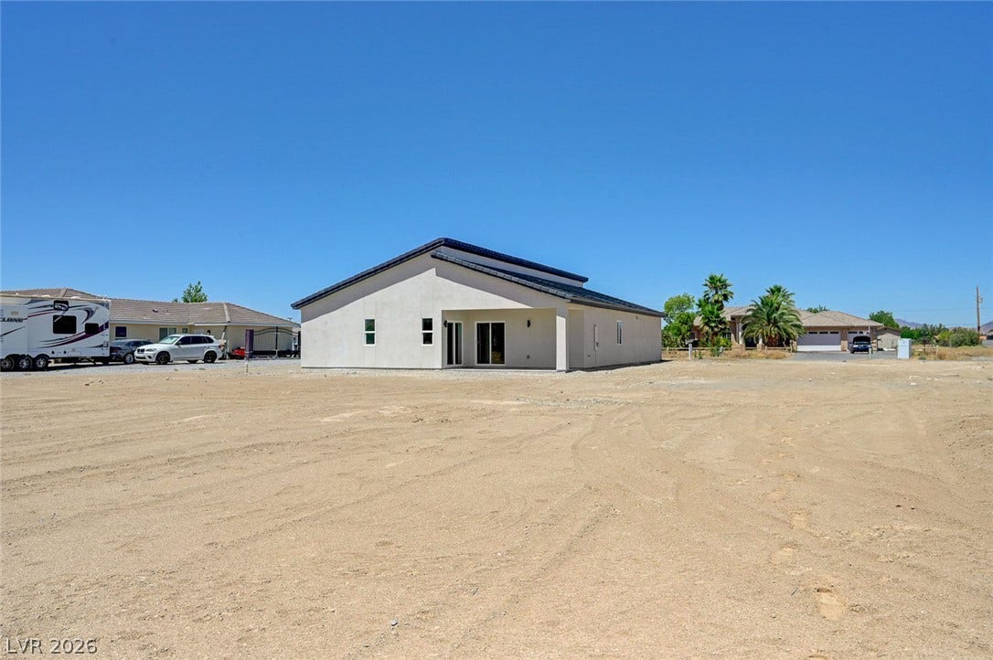 A spacious unimproved dirt yard stretches behind this modern stucco home.