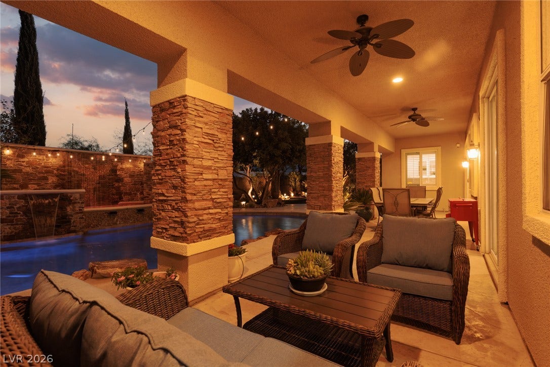 9795 Amador Ranch Avenue, Las Vegas, NV 89149 A spacious covered patio with stone-accented pillars overlooks a private swimming pool at sunset.