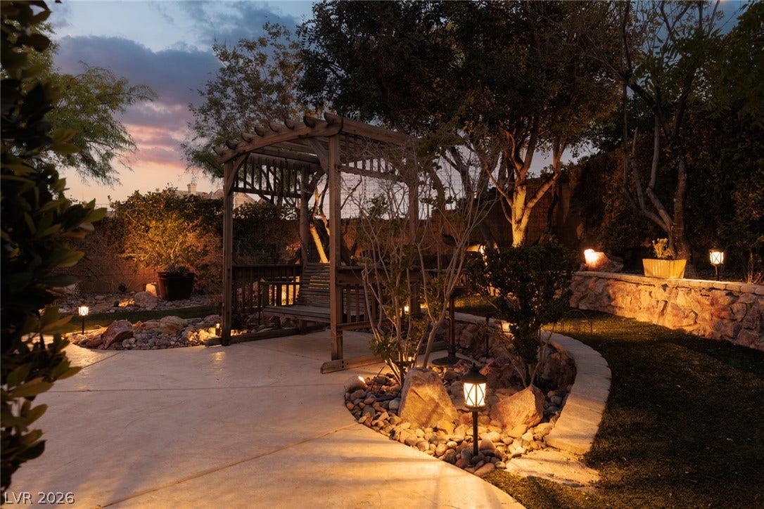 9795 Amador Ranch Avenue, Las Vegas, NV 89149 A stone retaining wall and concrete patio frame this landscaped backyard with a wooden pergola.