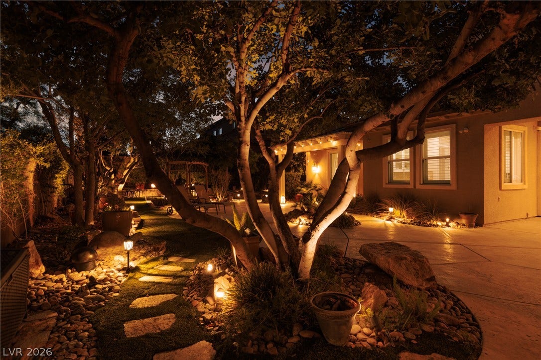 9795 Amador Ranch Avenue, Las Vegas, NV 89149 Lush landscaping and custom outdoor lighting create a magical evening ambiance across the grounds.