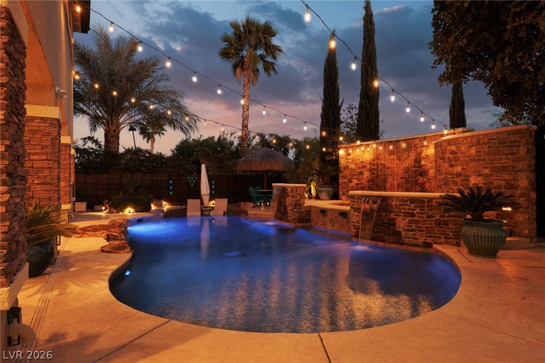 9795 Amador Ranch Avenue, Las Vegas, NV 89149 Stone walls and multiple waterfalls frame the illuminated swimming pool under a twilight sky.