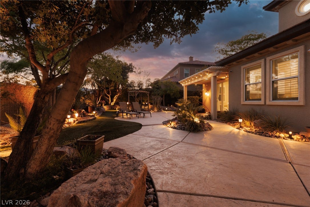 9795 Amador Ranch Avenue, Las Vegas, NV 89149 Artfully illuminated concrete pathways wind through a landscaped yard under a warm twilight sky.