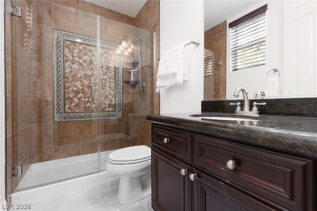 9795 Amador Ranch Avenue, Las Vegas, NV 89149 Richly tiled walk-in shower pairs with a dark vanity topped in polished stone.