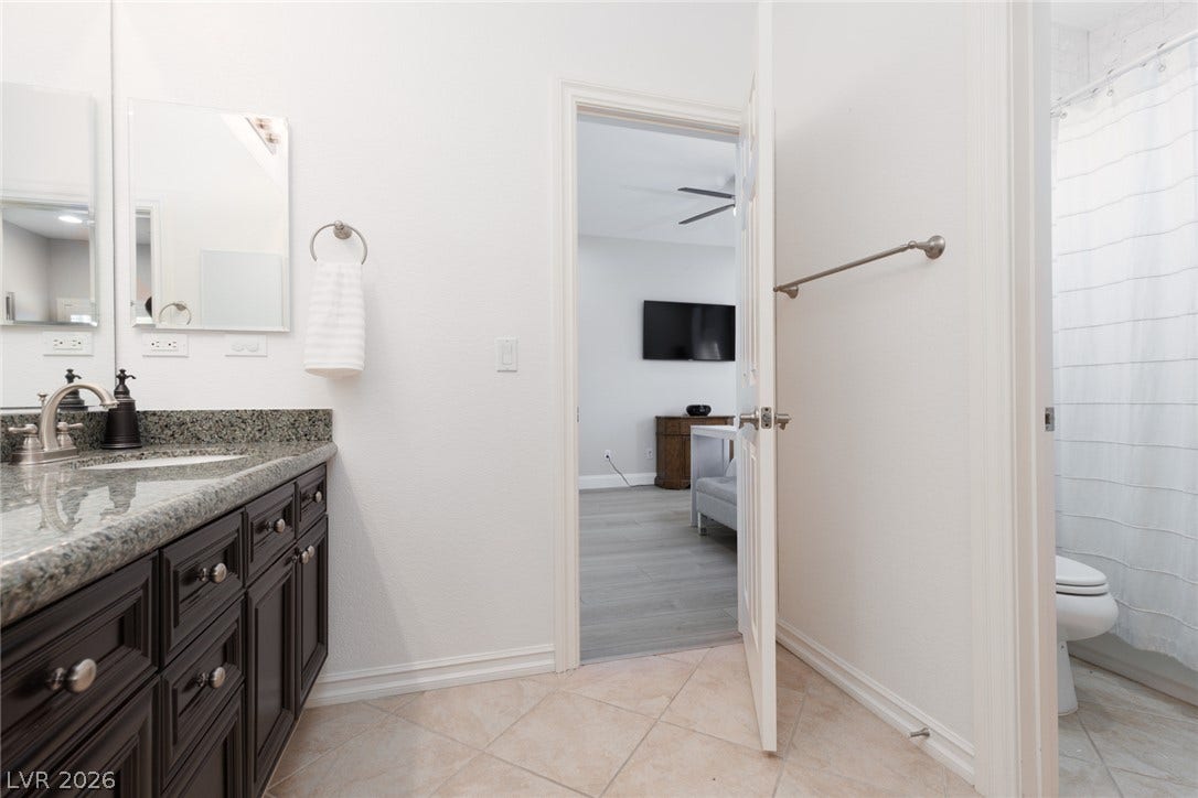 9795 Amador Ranch Avenue, Las Vegas, NV 89149 Polished granite countertops complement dark wood cabinetry and neutral tile flooring in this bathroom.