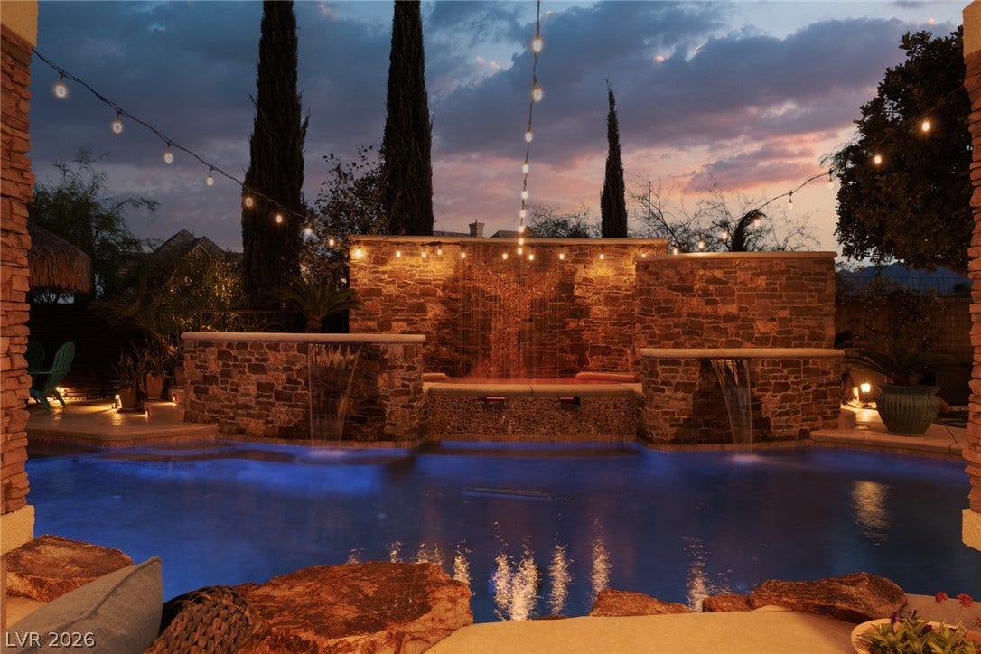 9795 Amador Ranch Avenue, Las Vegas, NV 89149 An inviting backyard pool features beautiful stone waterfalls glowing under an evening sky.
