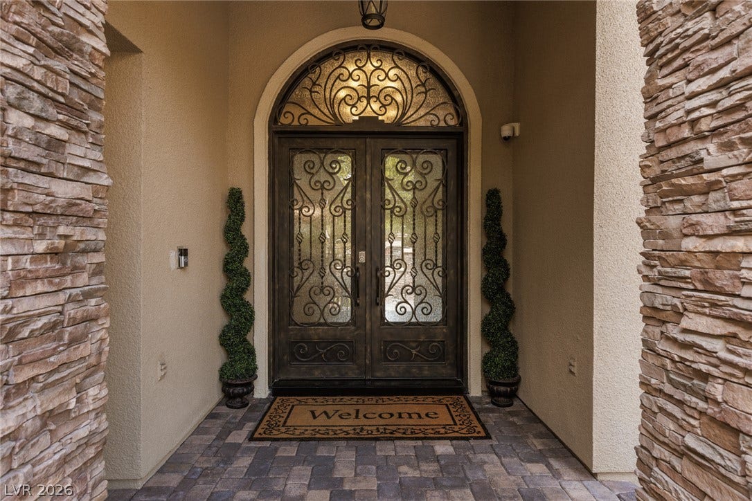 9795 Amador Ranch Avenue, Las Vegas, NV 89149 An arched entry with ornate double doors and stone accents creates a grand arrival.