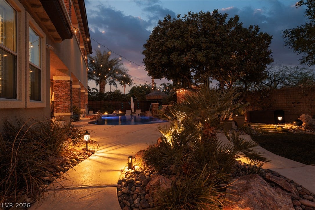 9795 Amador Ranch Avenue, Las Vegas, NV 89149 Lush landscaping and custom stone accents frame this private backyard pool oasis under evening skies.