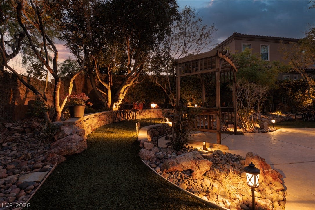 9795 Amador Ranch Avenue, Las Vegas, NV 89149 Artful landscape lighting illuminates a manicured lawn, stone retaining walls, and a wooden pergola.
