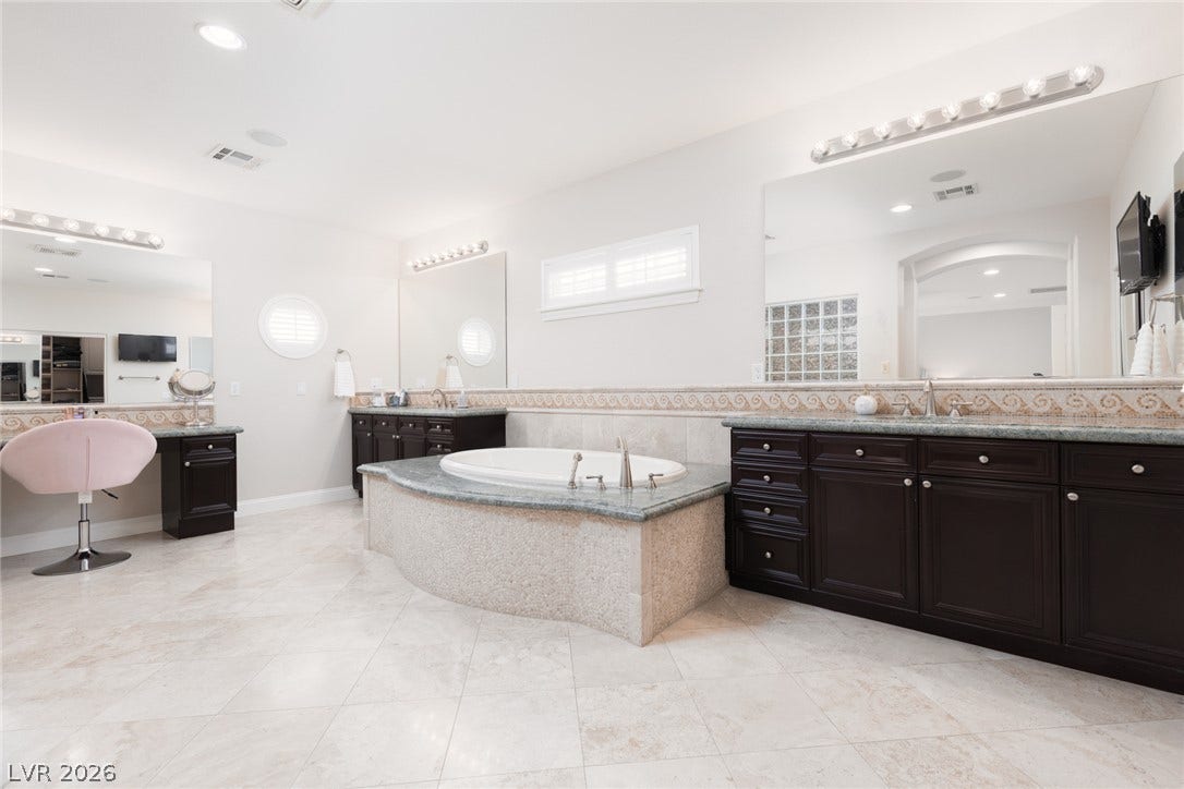 9795 Amador Ranch Avenue, Las Vegas, NV 89149 Plentiful custom cabinetry and a deep soaking tub anchor this tile-floored primary bathroom.