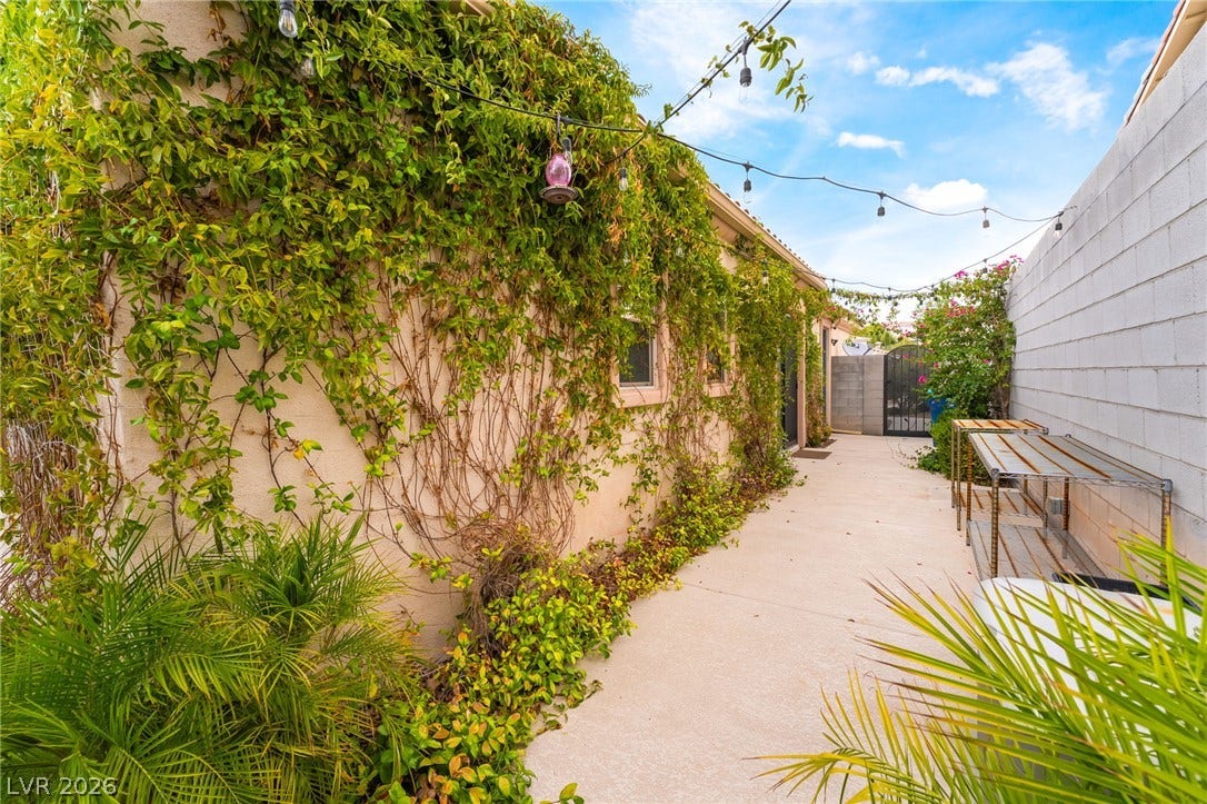 3033 Via Meridiana, Henderson, NV 89052 Lush ivy climbs stucco walls alongside a paved side walkway leading to a gated entry.