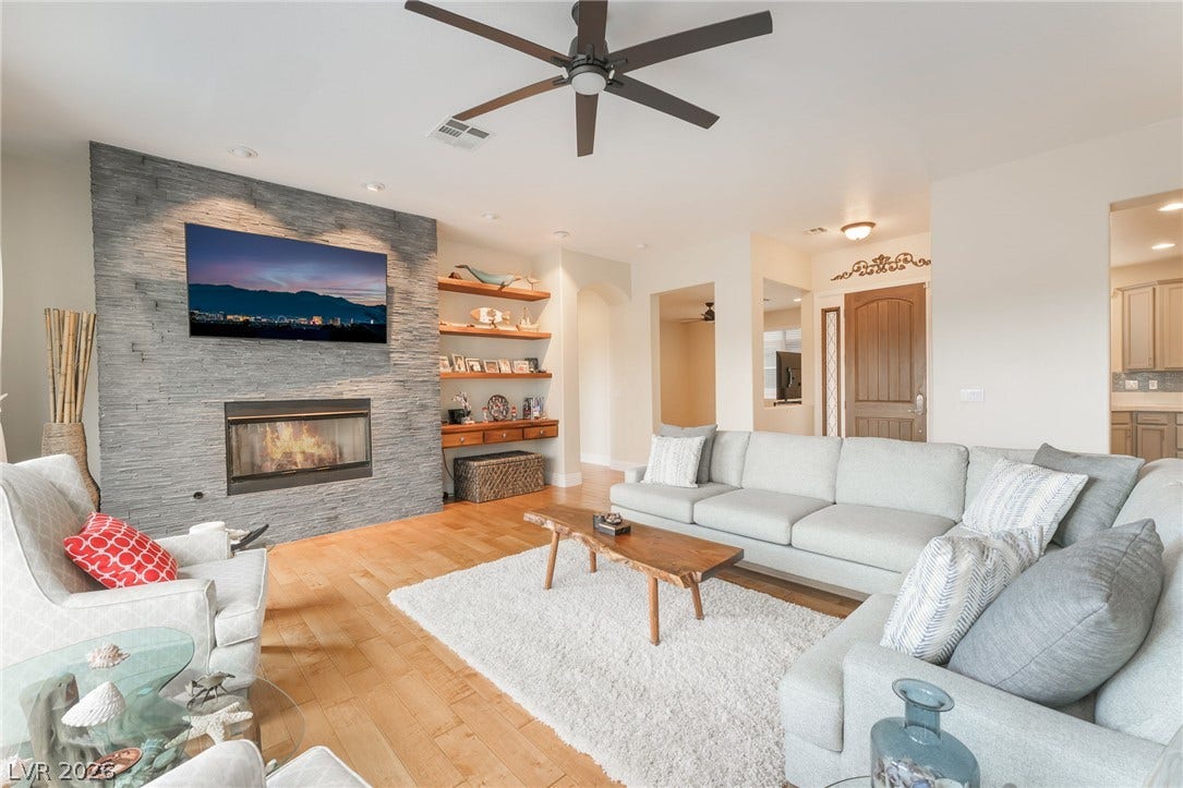 3033 Via Meridiana, Henderson, NV 89052 A stone fireplace anchors the living room featuring light hardwood flooring and recessed lighting.