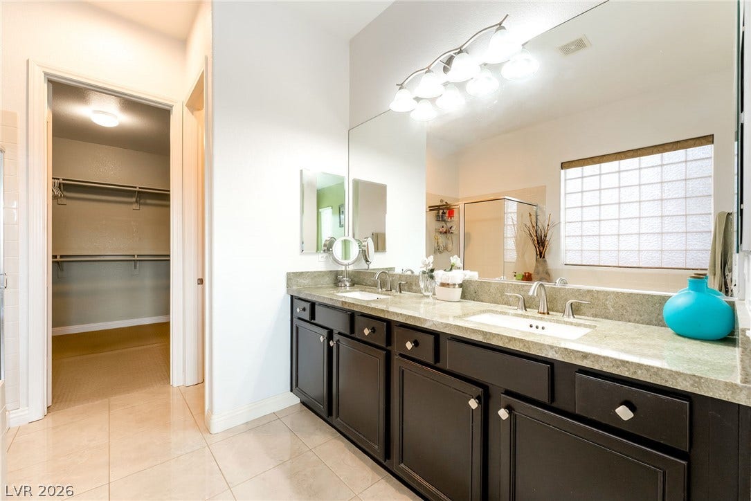 3033 Via Meridiana, Henderson, NV 89052 Polished tile flooring and dual vanities anchor this spacious bathroom alongside a walk-in closet.
