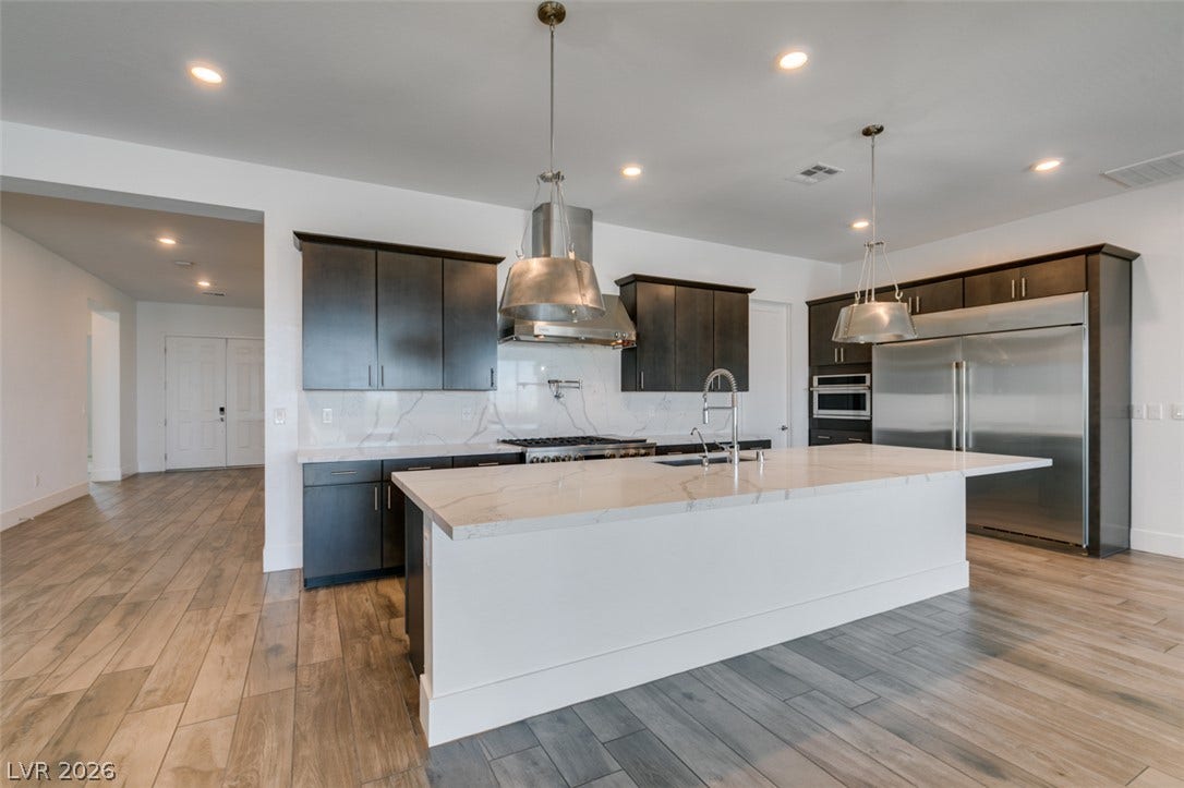 11288 Rebel Dome Court, Las Vegas, NV 89141 Rich dark cabinetry and polished stone countertops elevate this airy open-concept kitchen.