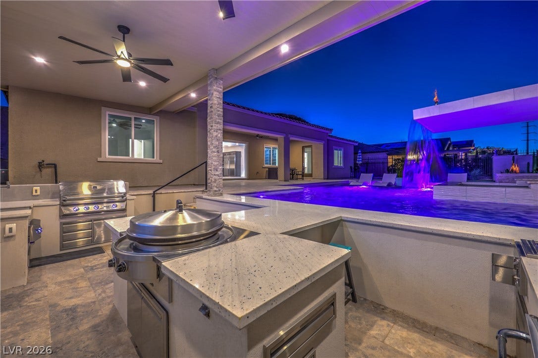 11288 Rebel Dome Court, Las Vegas, NV 89141 An integrated outdoor kitchen overlooks a private pool with a custom waterfall feature under twilight skies.