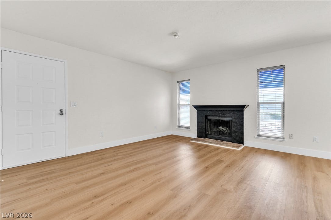 Smooth wood floors anchor this open space featuring a dark brick fireplace flanked by windows.