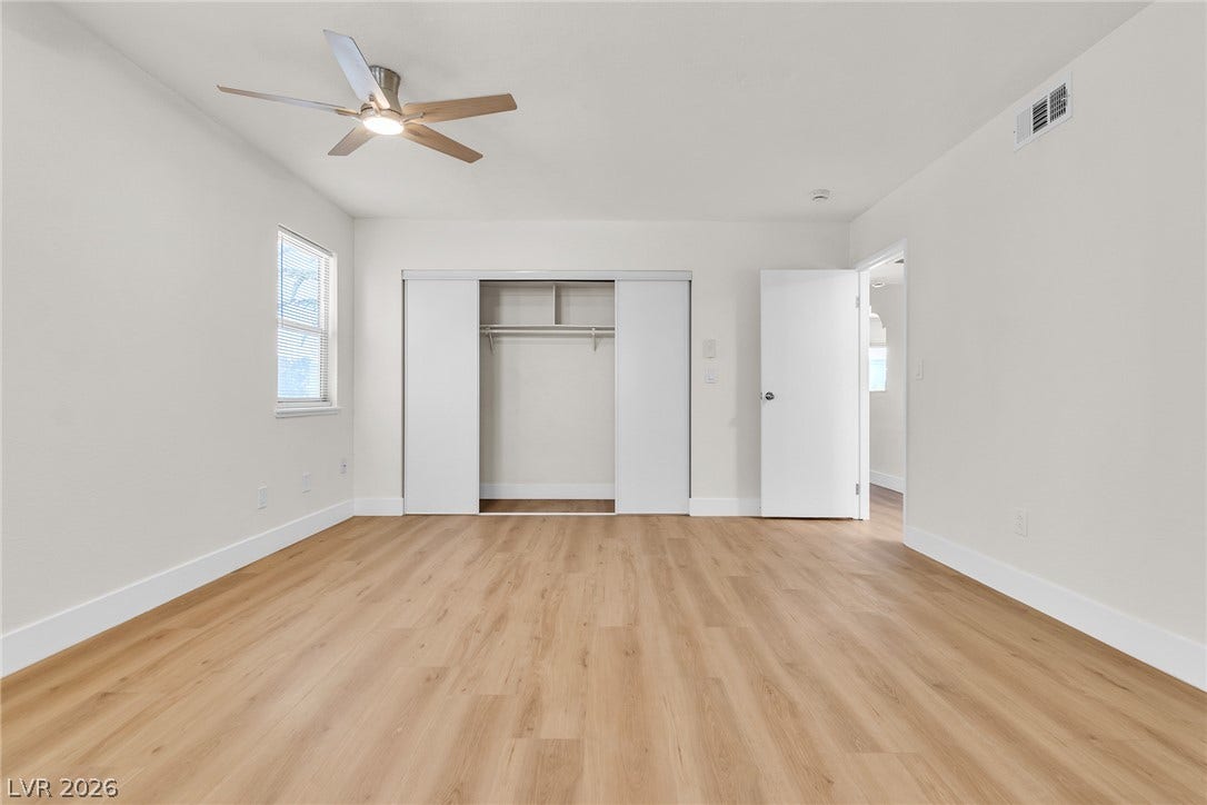 Smooth wood-style flooring runs throughout this clean bedroom featuring a generous sliding-door closet.