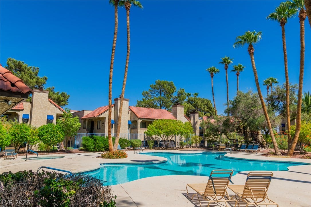 Manicured palms frame a refreshing community swimming pool set against tile-roofed residences.