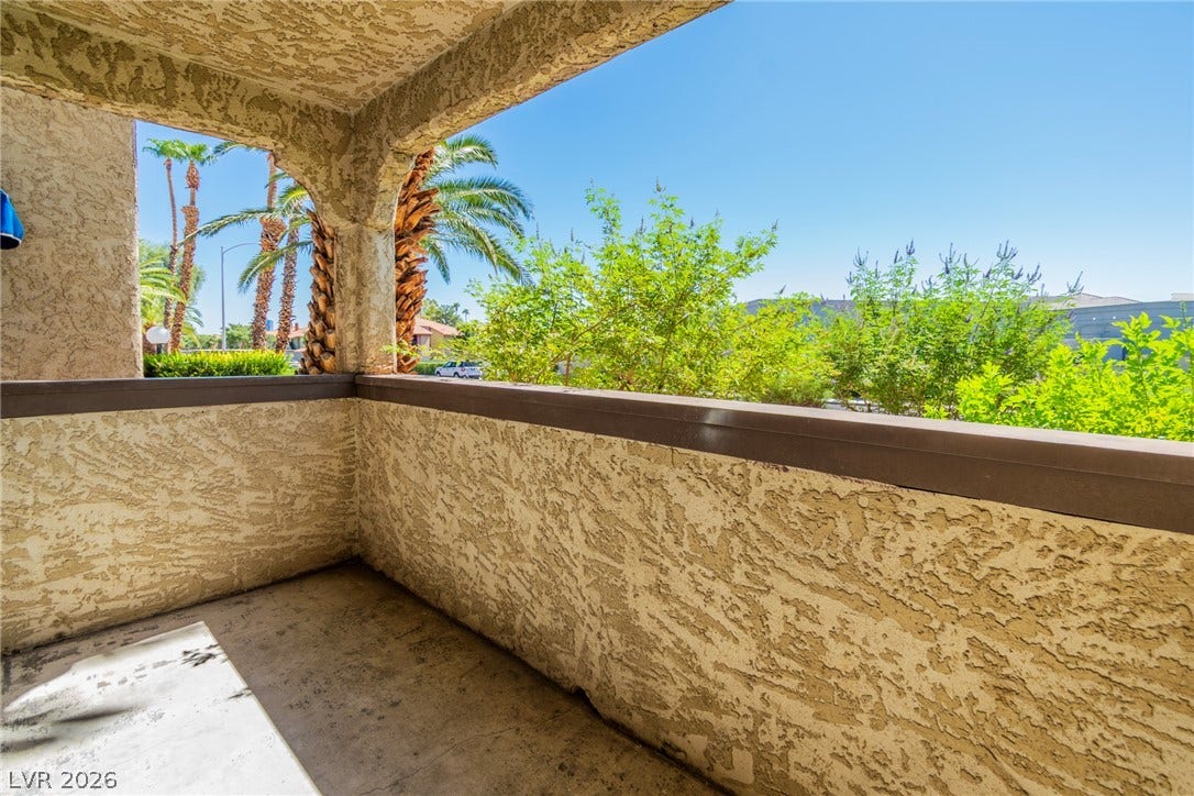 A private covered balcony overlooks lush green foliage and soaring palm trees.