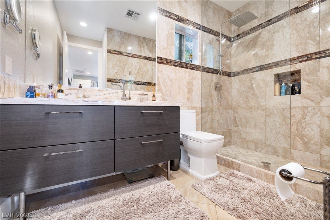 9624 Grand Isle Lane, Las Vegas, NV 89144 Floor-to-ceiling stone tile surrounds a glass-enclosed walk-in shower adjacent to a modern vanity.