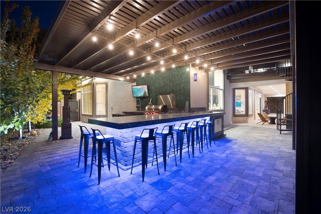 9624 Grand Isle Lane, Las Vegas, NV 89144 An inviting covered patio features a stone-wrapped outdoor kitchen, built-in barbecue, and paver flooring.