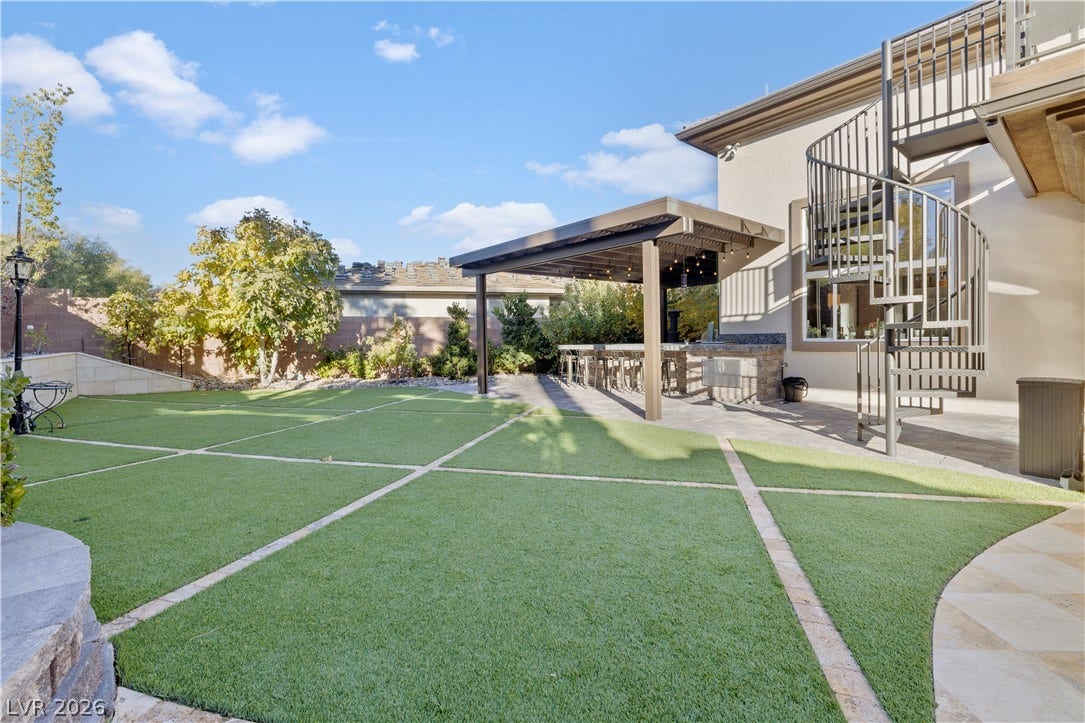 9624 Grand Isle Lane, Las Vegas, NV 89144 An inviting backyard oasis features a manicured lawn alongside an elegant outdoor kitchen setup.
