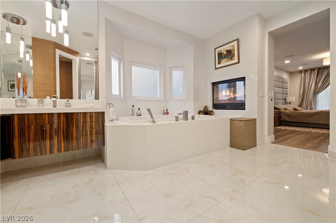 9624 Grand Isle Lane, Las Vegas, NV 89144 A double-sided fireplace warms this elegant bathroom complete with a soaking tub and stone flooring.