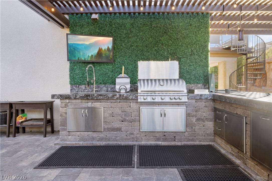 9624 Grand Isle Lane, Las Vegas, NV 89144 An outdoor kitchen features durable stone masonry, built-in stainless steel appliances, and a shaded pergola structure.