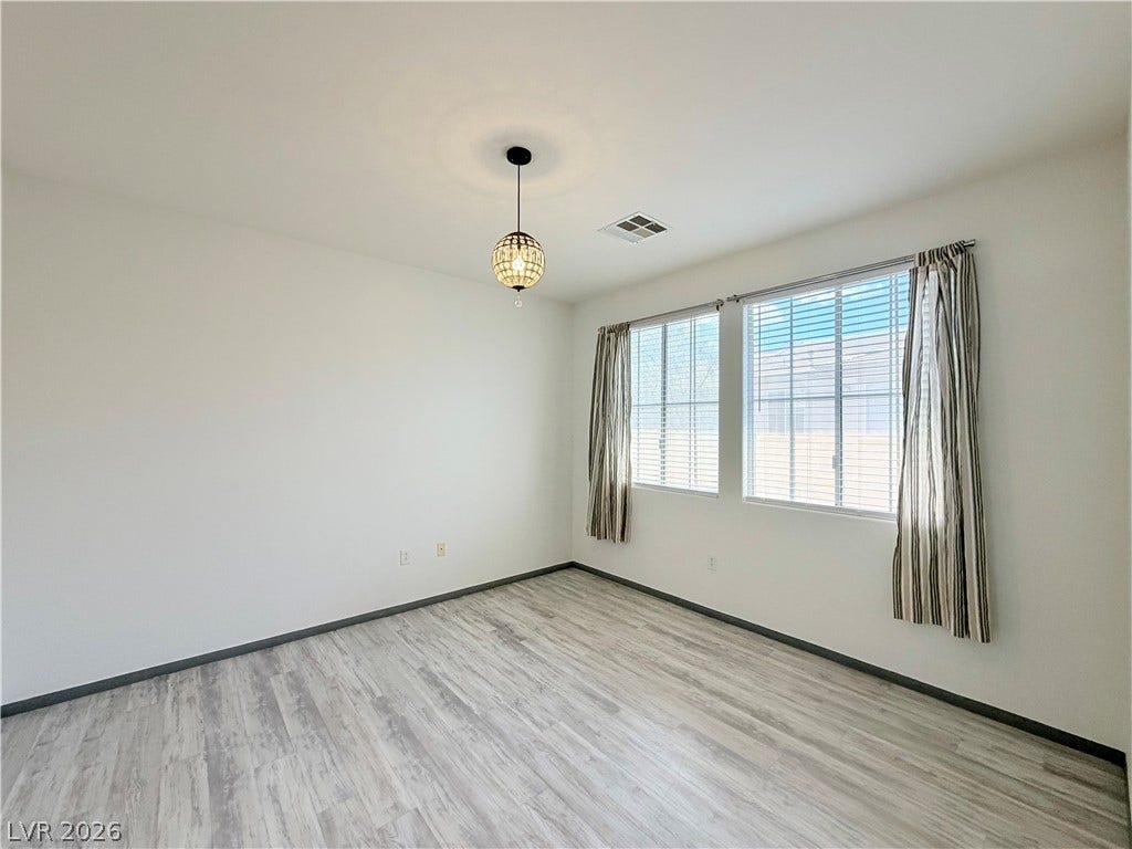 10221 Deerfield Beach Avenue, #202, Las Vegas, NV 89129 Laminate flooring sweeps across this versatile bedroom featuring tall windows and clean white walls.