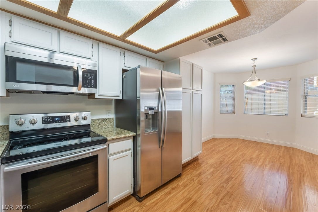 1305 Markwood Circle, #102, Las Vegas, NV 89128 Kitchen with stainless steel appliances, light wood finished floors, light stone counters, and white cabinetry