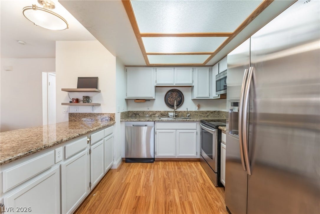 1305 Markwood Circle, #102, Las Vegas, NV 89128 Kitchen with stainless steel appliances, light wood finished floors, light stone counters, and white cabinetry