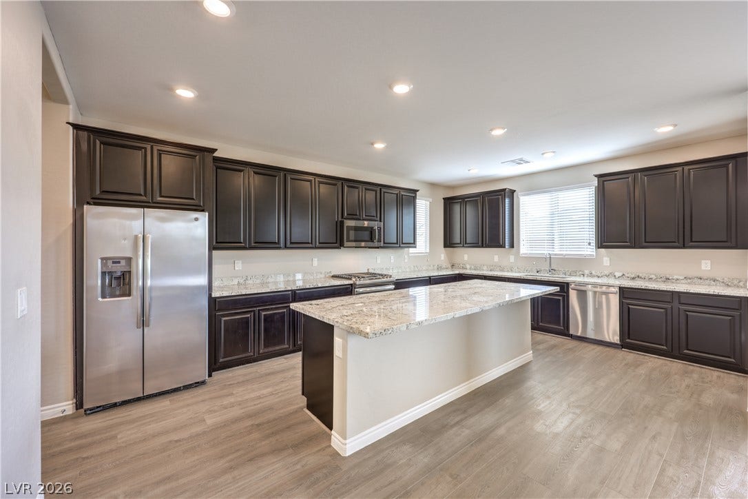 6934 Denio Island Street, North Las Vegas, NV 89084 Polished granite countertops and rich dark cabinetry elevate this spacious kitchen with central island.