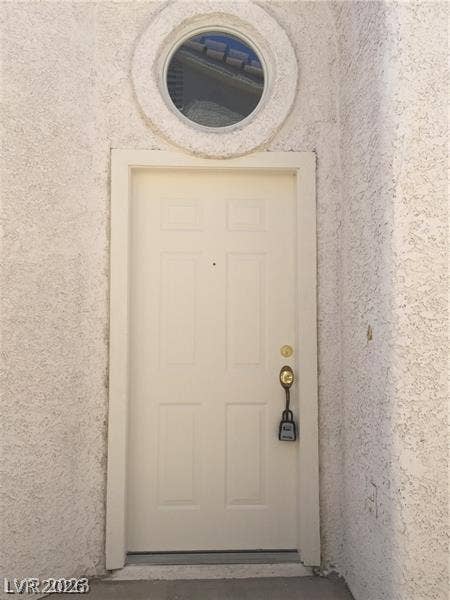 An arched entry recess pairs stucco textured walls with a circular transom window overhead.