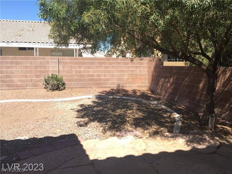 Mature trees cast cooling shade over a fully enclosed backyard with stone patio accents.